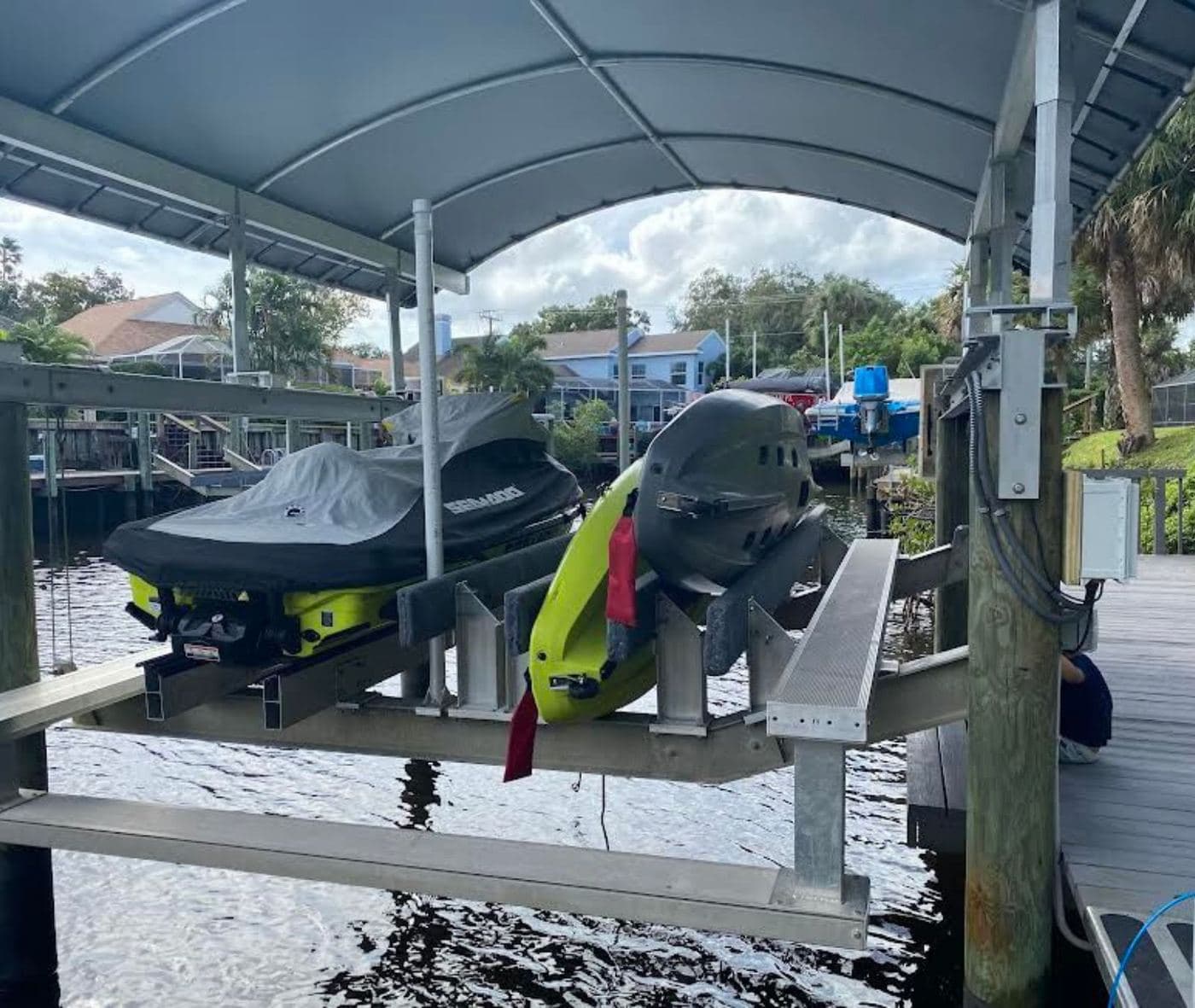 Jet skis on lifts under a covered boathouse with a metal roof