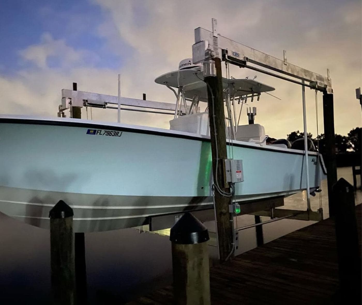 A center-console boat raised on a boat lift at dusk