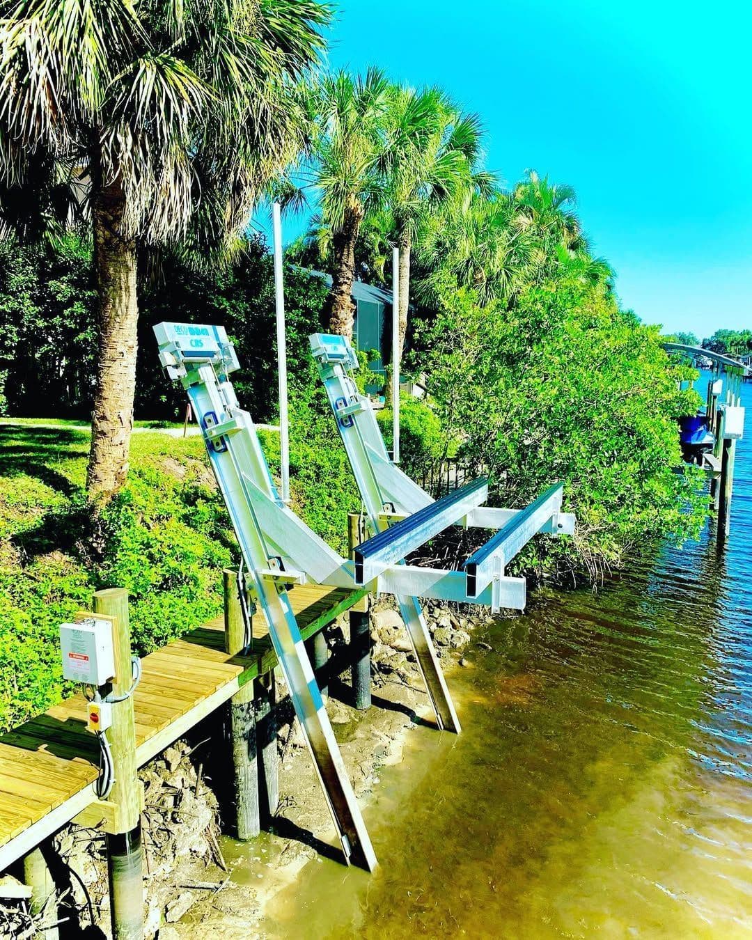 A boat lift standing in clear shallow water beside a palm-lined bank