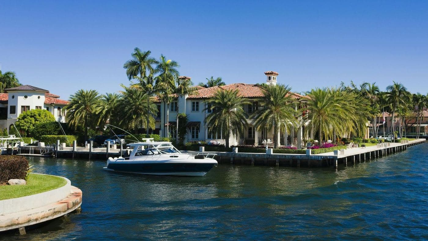 Waterfront homes with seawalls along a wide canal, with a boat passing