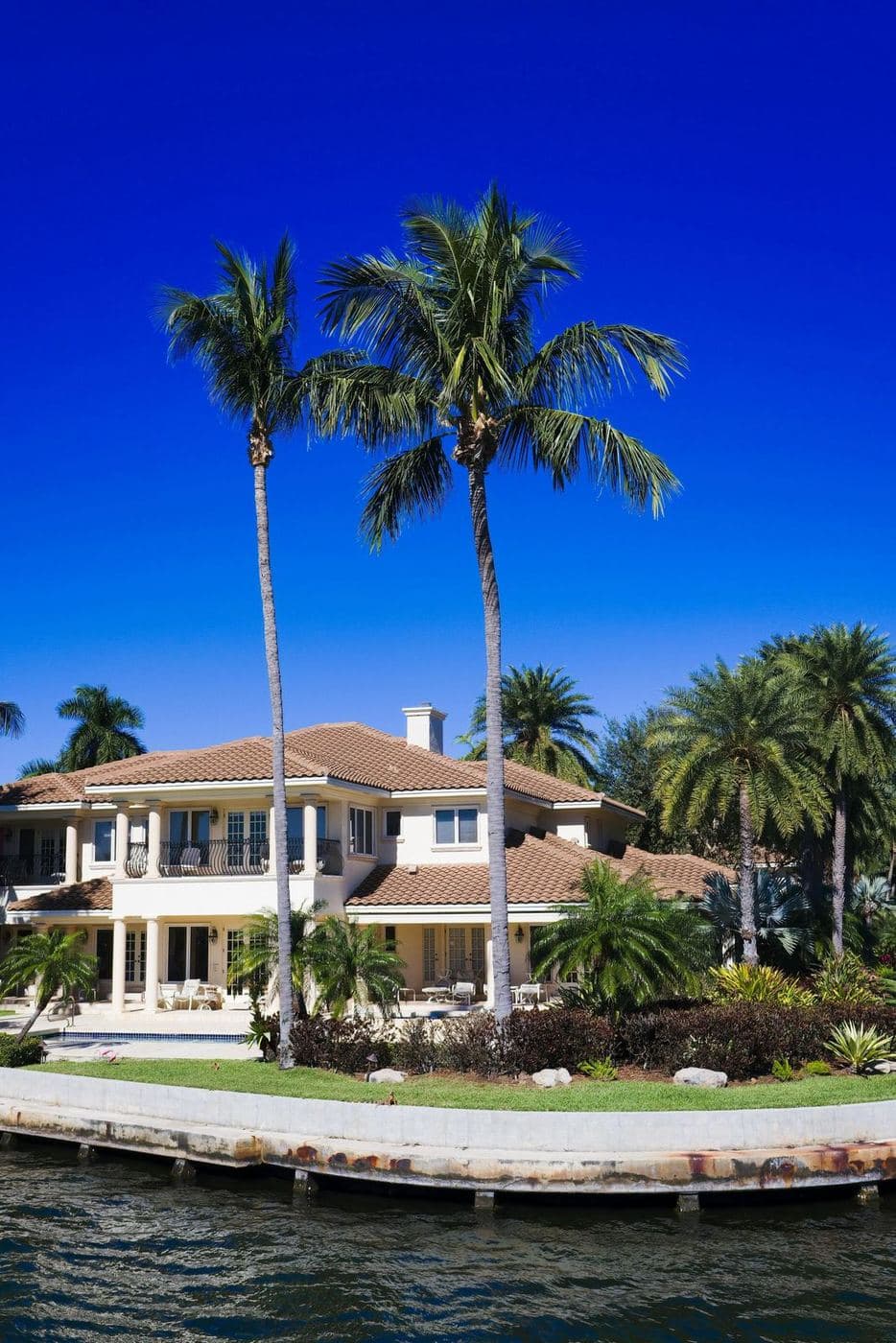 A waterfront home behind a seawall, framed by palms